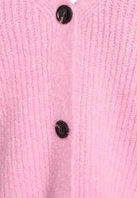 Tuvplāns no mīksta rozā adīta auduma ar divām melnām pogām, kas vertikāli iestrādātas virsmā.