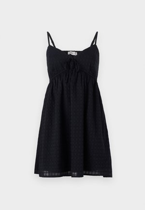 Juoda suknelė su plonomis petnešėlėmis, mazgo detale krūtinės srityje ir tekstūruotu raštu. Platėjantis, iki kelių siekiantis modelis su laisvu kirpimu.