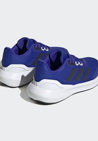 Scarpe da ginnastica viola con una tomaia in tessuto texturizzato, strisce nere a contrasto e suola bianca, dotate di un tallone imbottito per un supporto aggiuntivo.