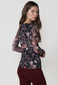 Top negro de flores de manga larga con mangas transparentes, que presenta un diseño de flores en tonos rosa y verde. Diseño ajustado con un sencillo escote redondo.
