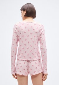 Ροζ μακρυμάνικη μπλούζα και αντίστοιχα σορτς με επαναλαμβανόμενο μοτίβο φιογκάκια, κατασκευασμένα από μαλακό ύφασμα, με άνετη γραμμή και ίσια τελείωμα.