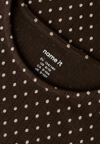 Brązowa dzianinowa koszulka w kremowe groszki, o prążkowanej fakturze i okrągłym dekolcie. Zawiera metkę pielęgnacyjną z informacjami o rozmiarze.