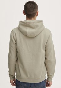 Felpa beige con cappuccio regolabile, polsini a costine e tasca a marsupio. Tessuto morbido, vestibilità casual e cuciture visibili lungo le cuciture.