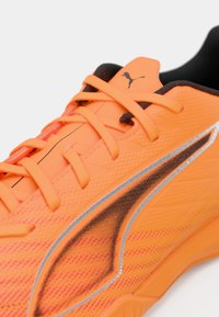 Scarpa sportiva con lacci di un vivace arancione, realizzata in materiale sintetico strutturato, con dettagli neri e rifiniture argentate riflettenti sul lato.