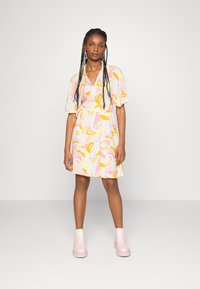 Vestido envolvente de mangas curtas em tecido rosa claro com padrões abstratos amarelos e laranjas. A modelo usa botas cano curto rosa chunk.