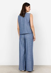 Blå ärmlös topp och matchande vida byxor, tillverkade av textil med en subtil mönstring, med minimalistiska designelement.