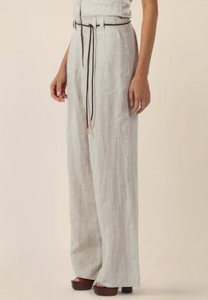 Frau trägt hellbeige weite Hosen mit einem dünnen schwarzen Gürtel, der in der Taille gebunden ist, kombiniert mit dunkelbraunen Plateausandalen.