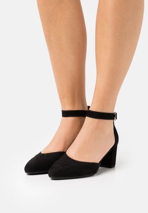 Black suede heeled shoes with an ankle strap. The shoes feature a pointed toe and a block heel. Smooth texture with minimal accents.