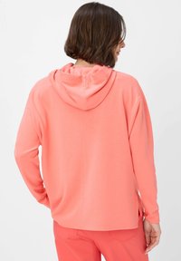 Felpa corallo con vestibilità rilassata, texture morbida e cappuccio con coulisse. Presenta maniche lunghe e un orlo arrotondato sul retro.