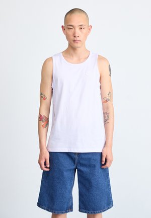 Lys lilla ermeløs tanktop laget av bomull, med en liten hvit logo. Satt sammen med blå denimshorts, som har en avslappet passform.