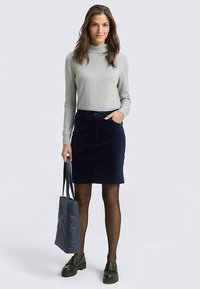 Pull à col roulé gris, jupe en velours côtelé bleu marine longueur genou, collants noirs, mocassins noirs et sac cabas bleu. Design simple et fonctionnel.