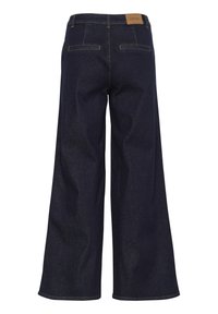 Valkoiset leveälahkeiset tummansiniset farkut, joissa on kaksi takataskua, vaaleanruskea nahkainen merkkilappu vyötäröllä ja kontrastoiva keltainen tikkaus.