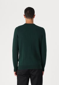 Suéter de malha verde escuro com mangas longas, bainha canelada e design de gola redonda, exibido em uma pessoa que veste calças pretas.
