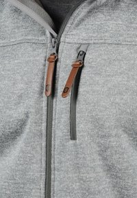 Veste zippée grise dotée de deux zips avant avec des tirettes en cuir marron, tissu texturé et doublure douce.