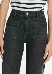 Zwart denim jeans met hoge taille, voorzakken, een knoopsluiting en zichtbare stiknaden. Materiaal heeft een gestructureerde afwerking voor duurzaamheid.