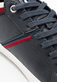 Baskets bleu marine foncé en cuir texturé, avec des bandes d'accentuation rouges et bleues, des lacets plats gris et une semelle en caoutchouc blanche.