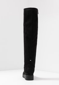 Bottes noires au-dessus du genou en daim, dotées d'une surface texturée et d'une fermeture éclair à l'arrière. La semelle est plate avec un talon minimal.