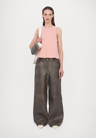 Top corto sin mangas de color rosa claro, pantalones de mezclilla gris-marrón de corte holgado con cremallera, y zapatos de tacón blanco puntiagudos, sosteniendo un bolso gris.
