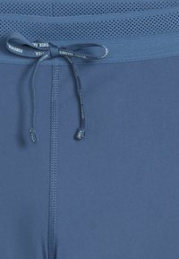 Shorts de sport bleus en tissu lisse, avec une taille en mesh et un cordon de serrage. Détails comprenant du texte imprimé sur le cordon.