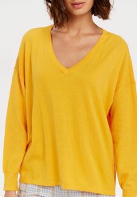 Pull jaune surdimensionné avec un col en V, manches longues, en tissu doux ; présente une coupe décontractée et une texture lisse.