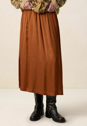 Femme portant une jupe midi marron avec une fente sur le côté, un cardigan imprimé léopard, et des bottes en cuir noir mi-mollet avec des boucles.