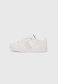White sneakers featuring a textured fabric upper with a geometric pattern, a beige accent strip, and a rubber sole. Text reads "MICHAEL KORS."