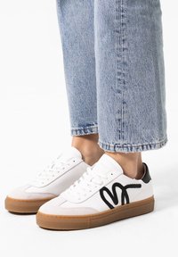 Weiße Sneakers aus Leder und Wildleder mit einem schwarzen Wellenmuster, Gummisohle und flachen Schnürsenkeln, getragen mit verkürzten blauen Jeans.