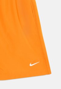 Orange Sport Shorts aus glattem Material. Mit einem weißen Nike-Logo in der unteren Ecke und weißen Nähten an den Seiten.