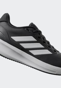 Chaussure de sport noire avec un dessus texturé, dotée de trois rayures blanches, d'une semelle légère et avec la marque "CLOUDFOAM" sur le côté.