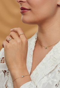 Ensemble de bijoux en or comprenant un collier délicat avec deux accents, un bracelet avec une pierre précieuse, et des bagues au design minimaliste.