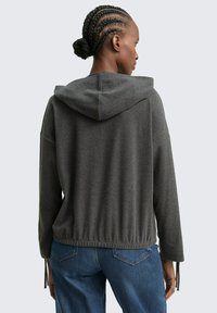 Grijze hoodie met een trekkoord onderkant en grote capuchon, gemaakt van zachte stof, met ingezakte schouders en een relaxte fit, gecombineerd met denim jeans.