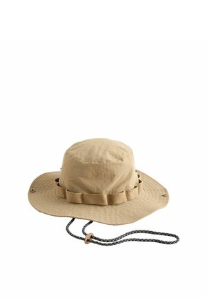 Beiger Outdoor-Sonnenhut mit breiter Krempe, verstellbarem schwarzem Kinnriemen und Stoffschlaufen um die Krone zum Befestigen von Accessoires.