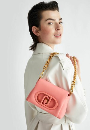 Sac à main synthétique rose avec une chaîne décorative dorée, arborant un logo bien en vue à l'avant et une texture lisse.