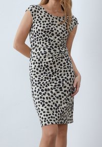 Robe à manches courtes, longueur genou, en tissu doux, avec un fond beige orné de grands pois noirs et un drapé léger à la taille.