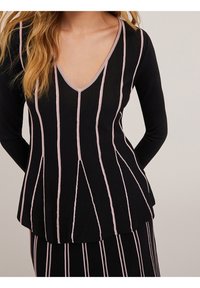 Musta neulepaita, jossa on pystysuoria vaaleanpunaisia raitoja, V-pääntie ja pitkät hihat, hieman levenevä helma ja sileä pinta.