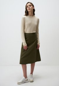 Crème, lange mouwen gebreide trui gecombineerd met een olijfgroene A-lijn midi rok en witte sneakers met beige accenten. Gladde textuur en eenvoudig ontwerp.