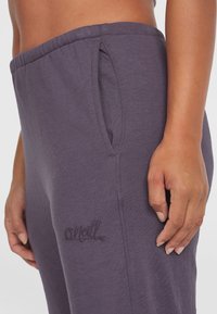 Pantaloni da tuta in cotone viola con tasche laterali e un sottile logo ricamato "O'Neill" sulla parte inferiore della gamba. Texture liscia e cintura elasticizzata.