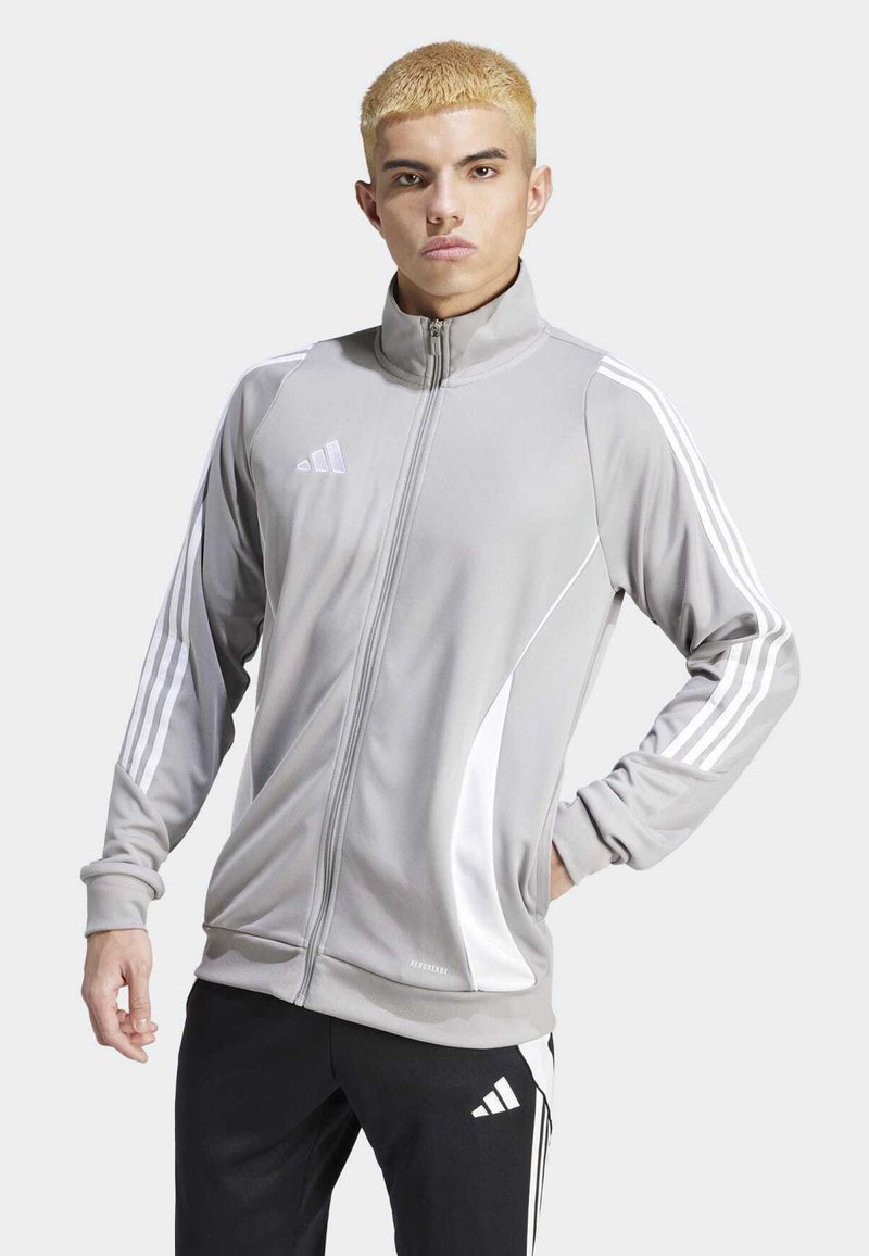 Grå atletisk jakke med lynlås, hvide detaljer og tredobbelt stribe langs ærmerne. Lavet af glat, let vævning.