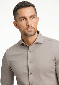 Camicia grigia a maniche lunghe con colletto button-down, patta centrale con bottoni e un tessuto morbido e testurizzato.