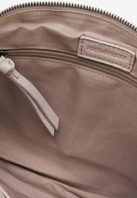 Interno di una borsa in tessuto beige con una texture liscia, dotata di una tasca con zip e un'etichetta contrassegnata "FREDSBRUDER". I dettagli includono un tirazip in pelle.