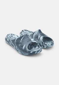 Kék és fehér álcázott slip-on szandál, nyitott orral és texturált talprésszel. Rugalmas anyagból készült, sima felülettel.