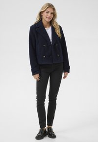 Veste double boutonnage en mélange de laine bleu marine avec un col cranté, de gros boutons et un tissu texturé ; associée à un pantalon noir slim et des mocassins.