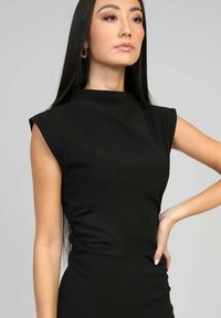 Robe noire sans manches avec un col haut, texture lisse et silhouette ajustée. Présente un léger ruché sur les côtés.