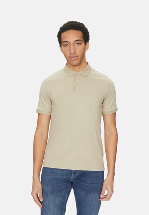 Camisa polo beige de tejido suave con cuello clásico, botón de tres botones y mangas cortas, combinada con unos vaqueros azules.