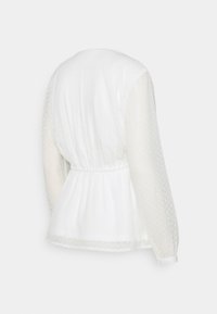 Blusa bianca con maniche lunghe a sbuffo in tessuto testurizzato, vita arricciata e motivo a pois su tessuto semi-trasparente. Vista posteriore mostrata.