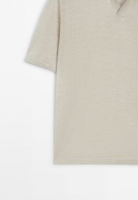 Polo en maille beige à manches courtes avec un col en V discret et une texture douce, présenté sur un fond blanc.