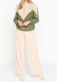 Suéter de punto verde y beige con diseño de zigzag, combinado con pantalones de pierna ancha crema con un acabado texturizado. Ajuste relajado en todo momento.