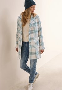 Rutigt ytterplagg i vitt och blått, med slagkrage, framfickor, som matchas med ljusblå jeans och vita sneakers.