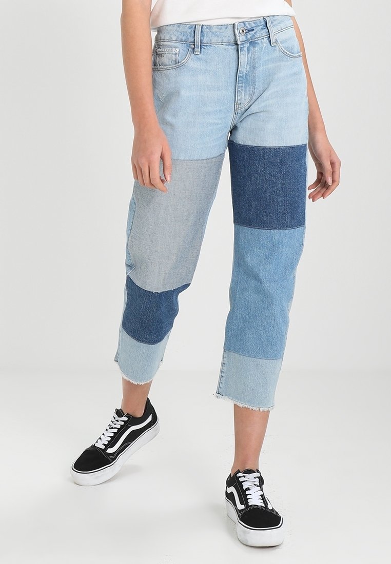 Ljusblå jeans med lapptäcktsdesign som har olika nyanser av denim. Kort längd med fransiga fållar, parat med svarta sneakers.