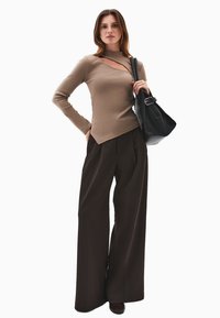 Beżowy dopasowany top z ukośnym wycięciem, w zestawieniu z szerokimi, ciemnobrowymi spodniami oraz czarną skórzaną torebką. Gładkie tekstury w całym zestawieniu.